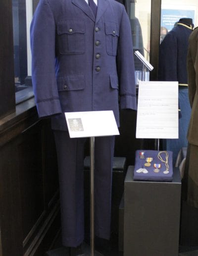 Image of a mannequin wearing an Air Force uniform consisting of a dark blue jacket, light blue button-up shirt, dark blue neck tie and dark blue pants.