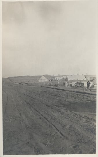 Rough dirt road in foreground extending to horizon. Large tents to right side of road.