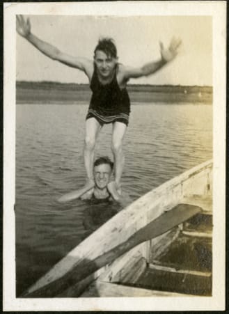Paddleboat in foreground in a lake. A man stands in lake with a boy standing on his shoulders.
