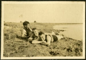 Three young men lay on the edge of a lake.